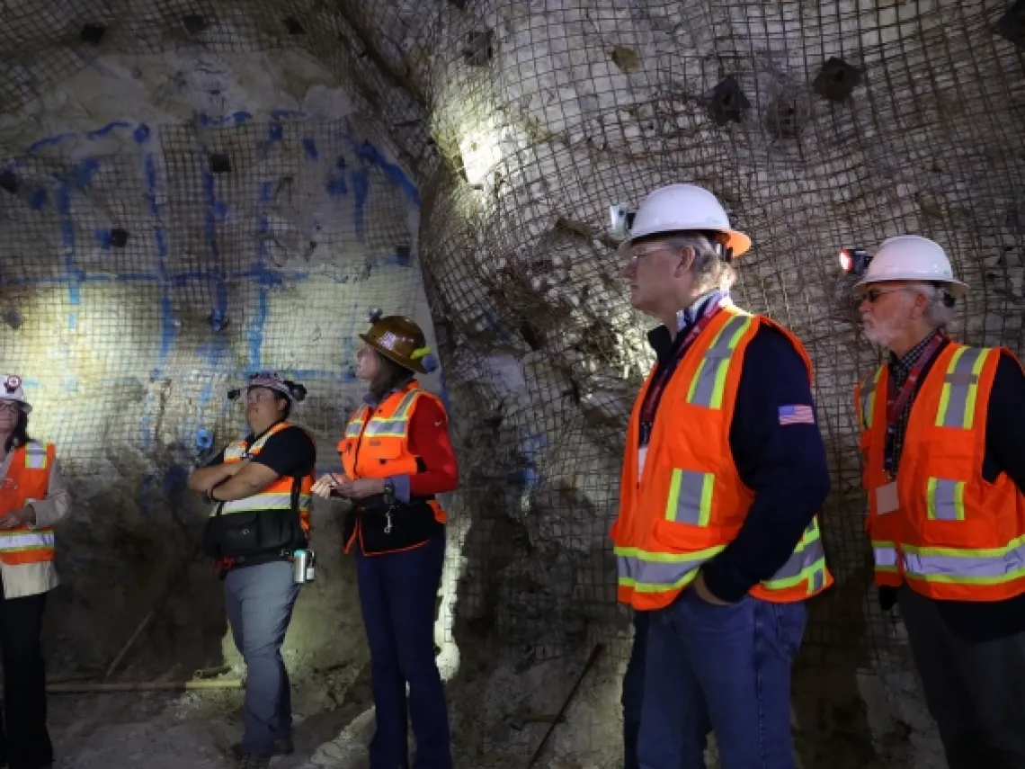 five people standing in a mine wearing orange vests and hard hats