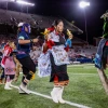 Hopi dancers performing a corn dance in traditional tribal clothing on a football field with stadium lights shining down
