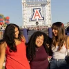 Three women smile and laugh in front of the Unviersity of Arizona logo.