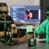 Wearing dark, tinted eye protection goggles, Willomitzer and a postdoctoral researcher set up instrumentation on an optical lab bench. 